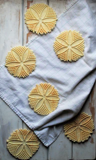 Delicate anise-flavored pizzelle cookies arranged in a circular pattern on a white plate.