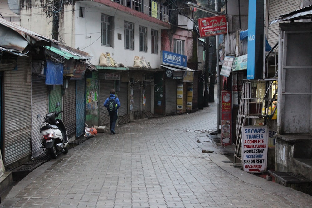 Persona in felpa con cappuccio blu che cammina per strada circondata da edifici