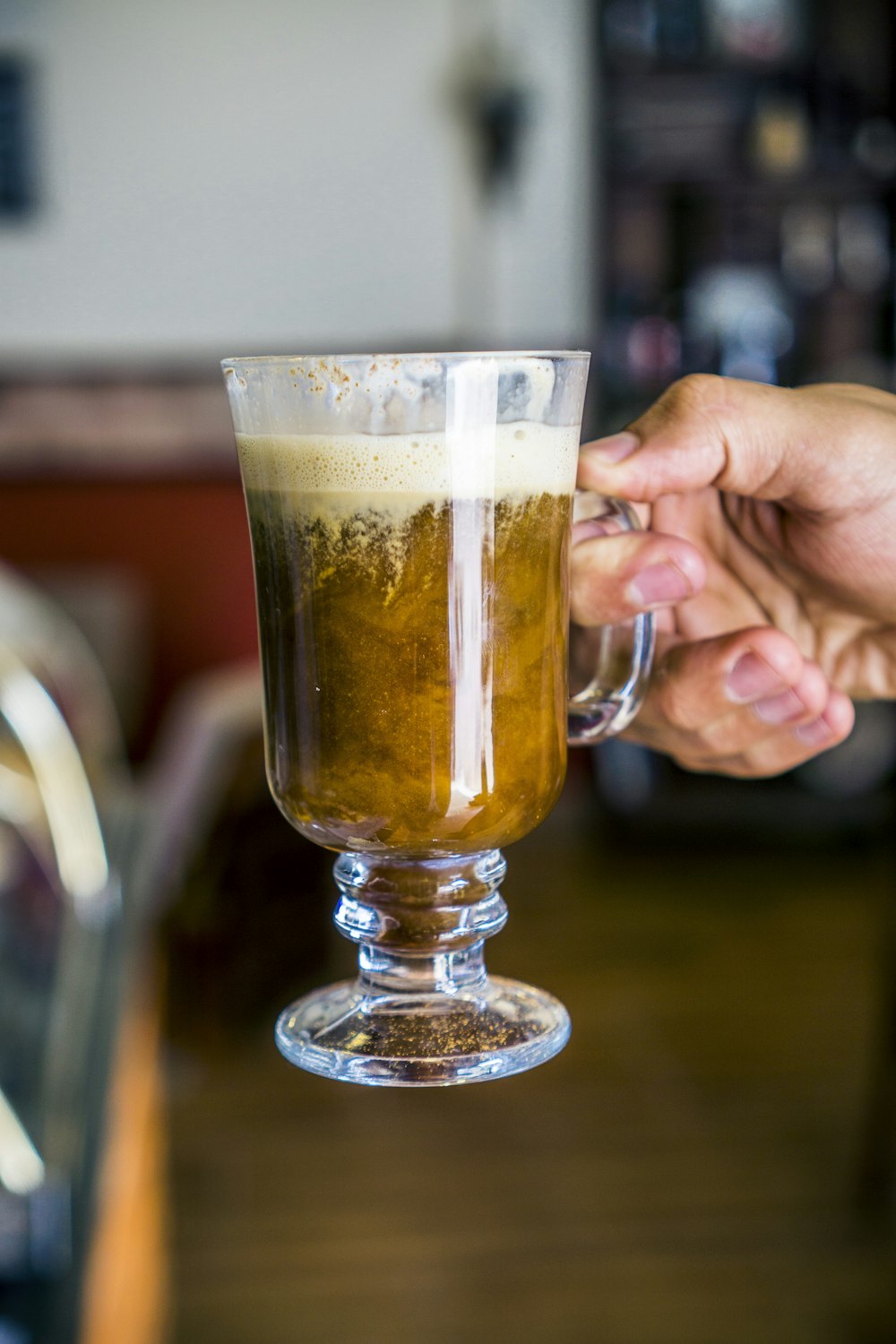 person holding glass mug with brown liquid