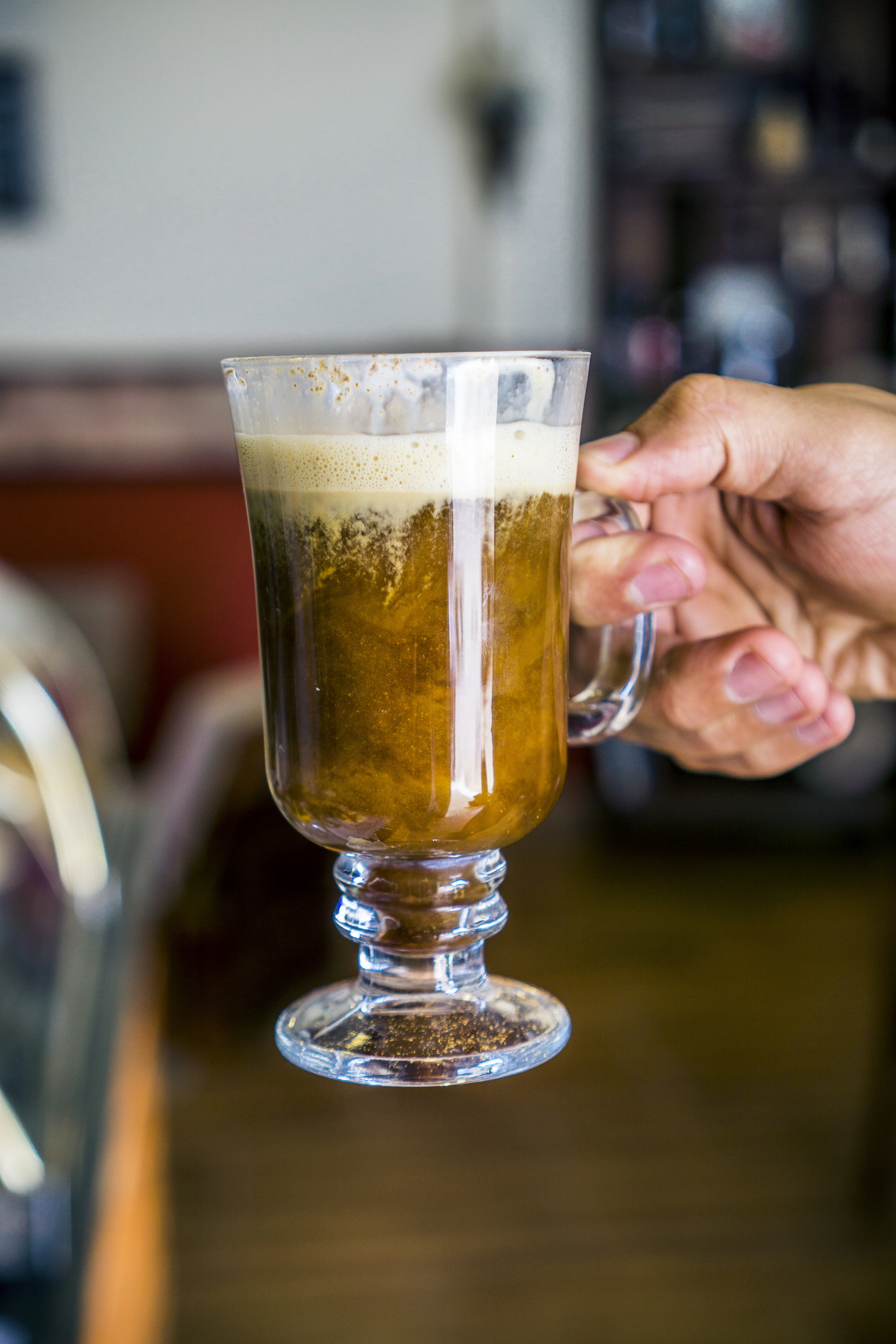 A glass of Irish coffee, cream floating on top, held in a warm pub interior