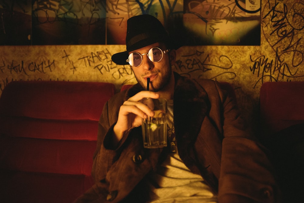 man holding glass cup while sitting on sofa