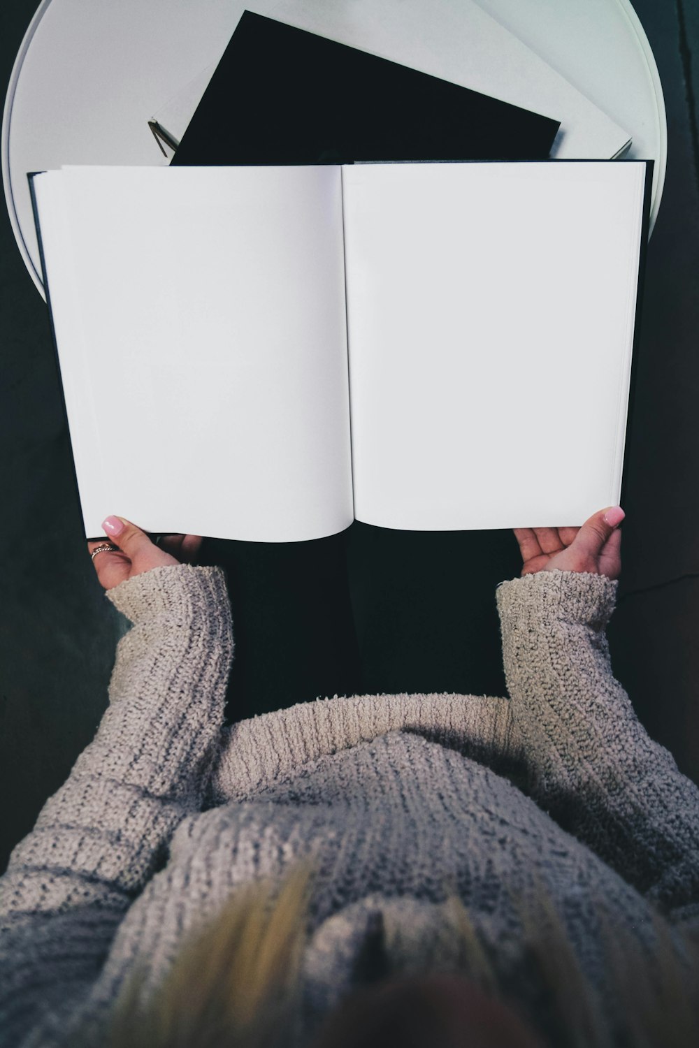 donna che indossa un maglione che apre un libro in bianco