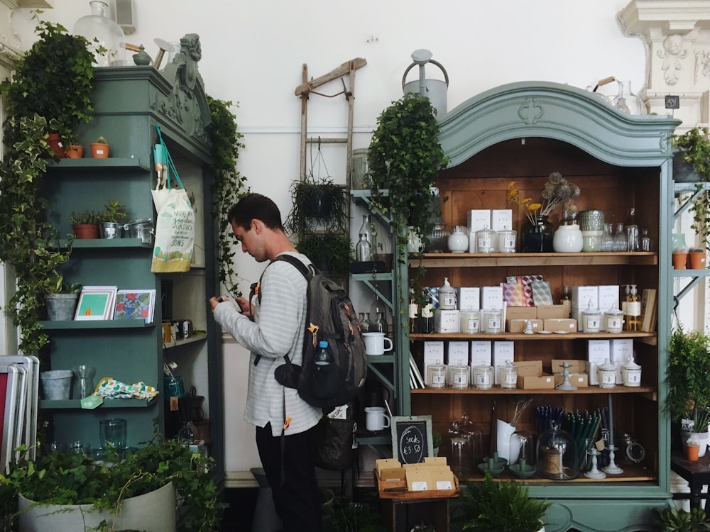 man in grey sweatshirt and brown backpack standing beside green wooden shelf