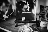 A black and white photograph is displayed on a small easel. The image captures an intimate moment between two people, and text overlay reads 'my soul will find yours.' Surrounding the photo are various objects, including a candle and tags, creating a cozy atmosphere.