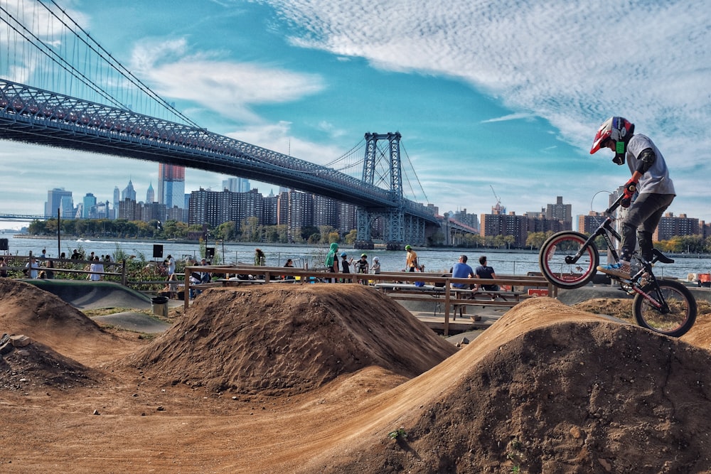 昼間、灰色の橋近くの土の斜面でBMXバイクに乗っている男性