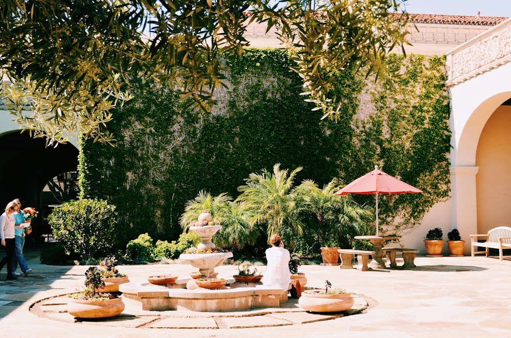 person sitting beside water foundation surrounded by trees