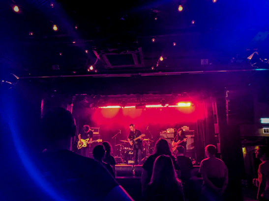 A moody photo of the band performing on stage with deep red lighting casting shadows.