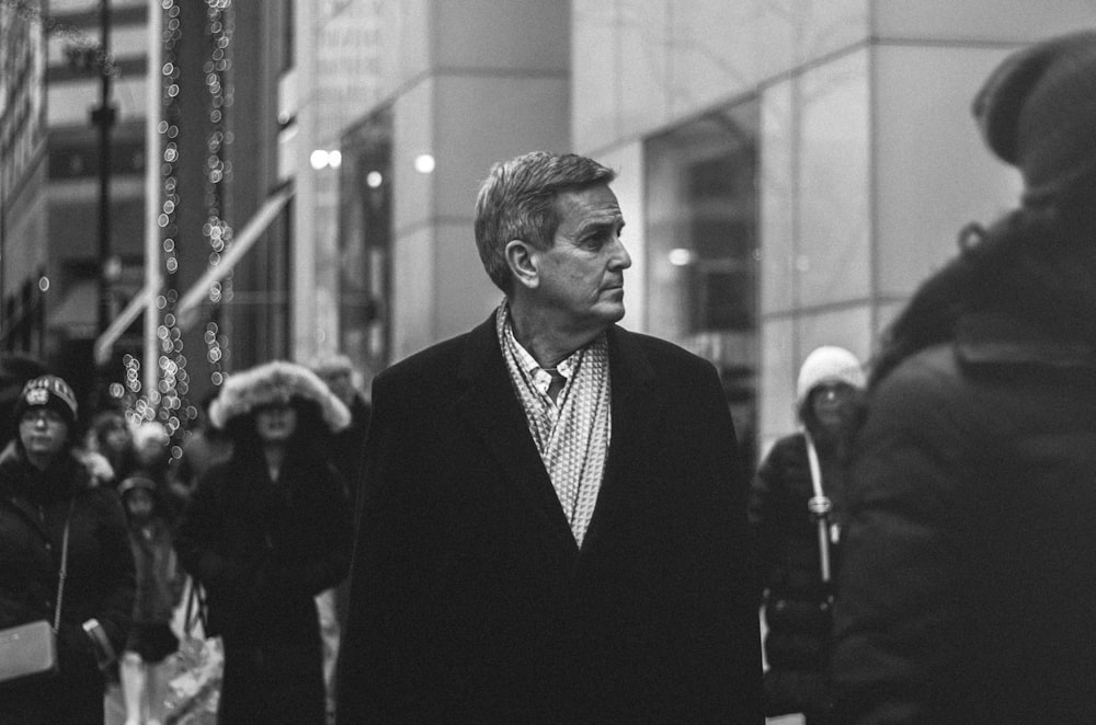 grayscale photography of a man walking while looking sideway