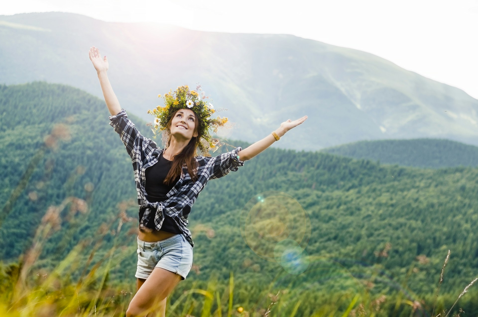 woman raising hands behind mountain covered by trees