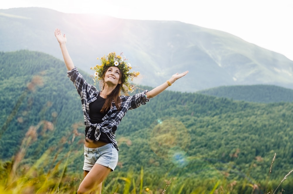 woman raising hands behind mountain covered by trees