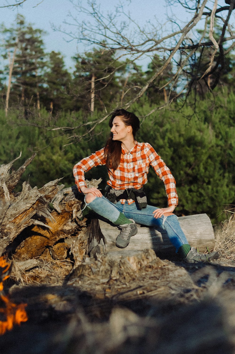 a woman sitting on top of a log next to a fire