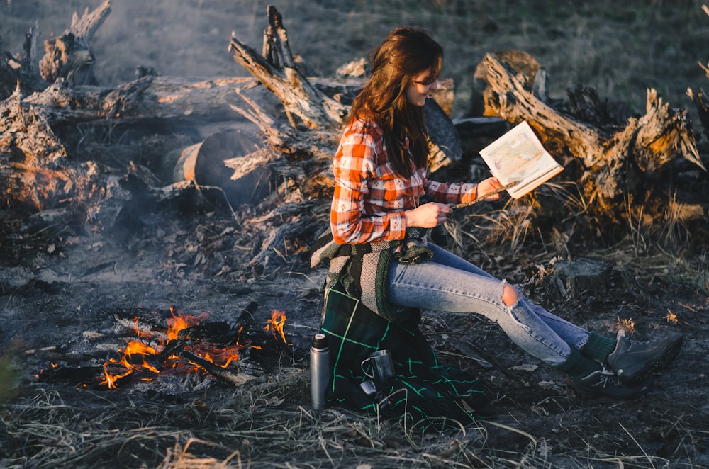 焚き火のそばで読書をしながら座っている女性