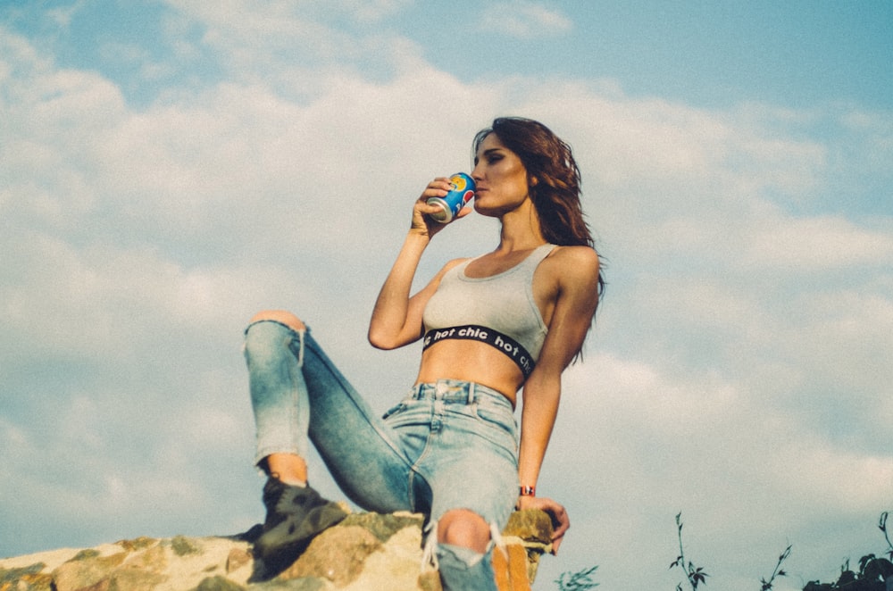 femme assise sur une colline rocheuse buvant une canette de soda pendant la journée