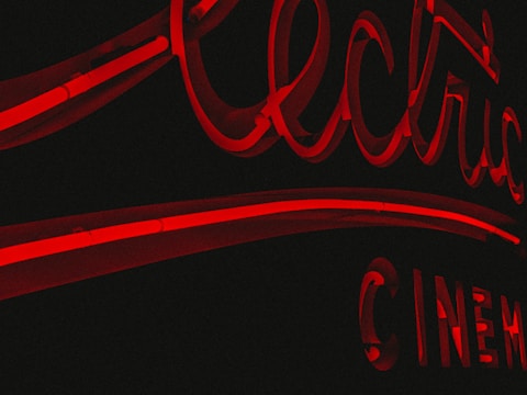 A moody cinematic scene illuminated by electric red neon highlights casting shadows over a film reel.