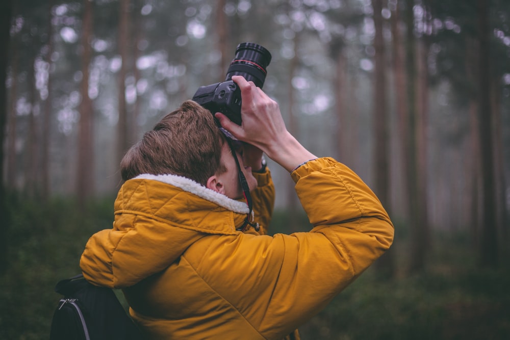 tilt-shift lens photography of man holding DSLR camera taking photo during daytime