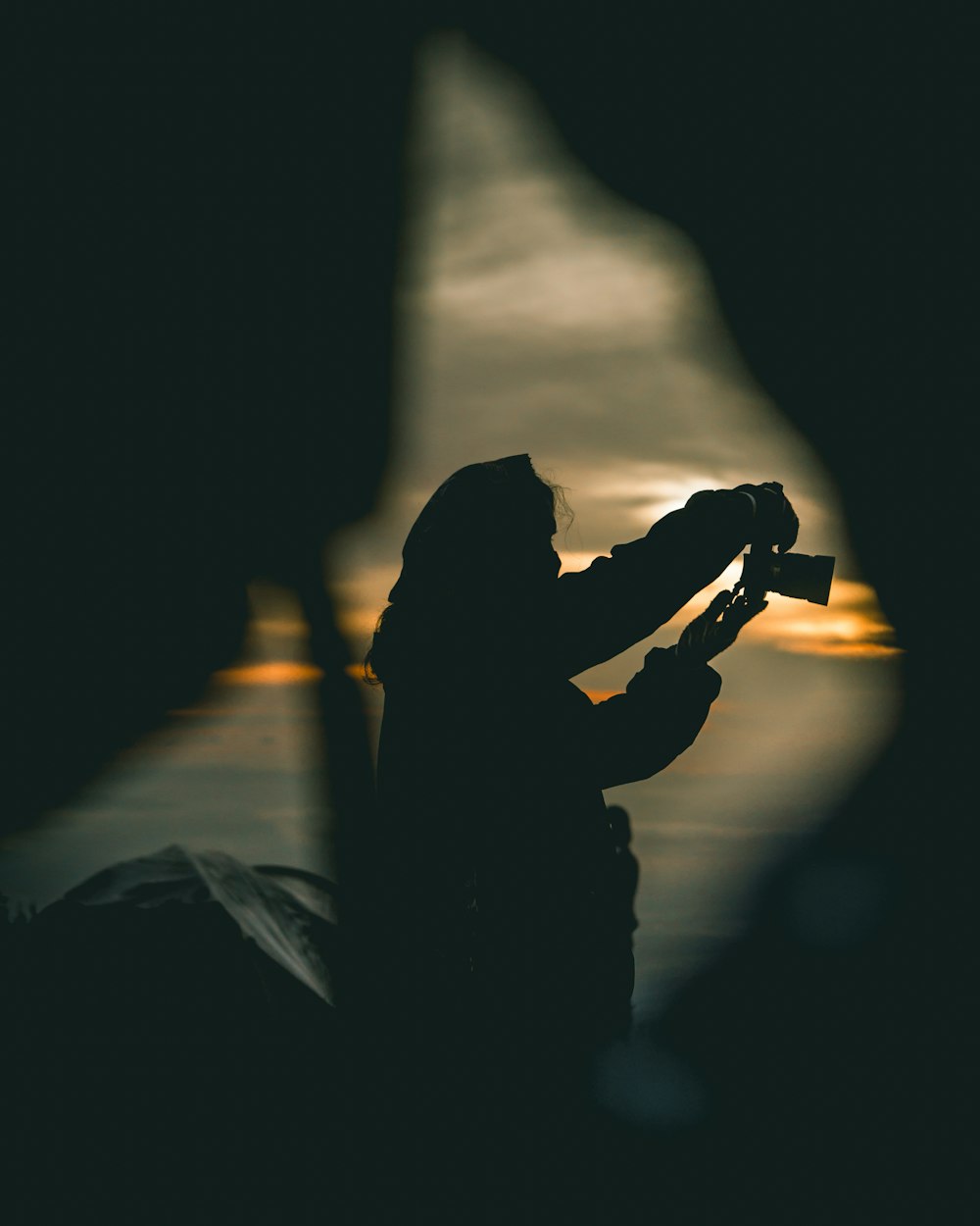 Silhouette einer Person, die während des orangefarbenen Sonnenuntergangs Kamera hält