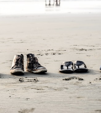two pair of shoes and flip-flops on seashore near people at daytime
