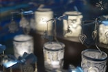 Ornately decorated candle holders with intricate metal designs hang, featuring shapes like horses and hearts. Soft light emanates from inside, casting gentle shadows and reflections, creating an ambient and cozy atmosphere.