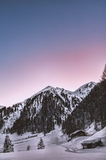 Cozy mountain lodge with snow-covered peaks in the background at sunset