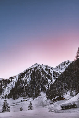 Cozy mountain chalet with snow-covered peaks in the background at sunset.