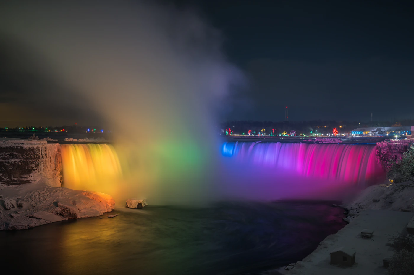 Niagara Falls at night illuminated by coloured lights with the falls glowing in blue and purple light and the mist rising in the darkness creating a dramatic nighttime image