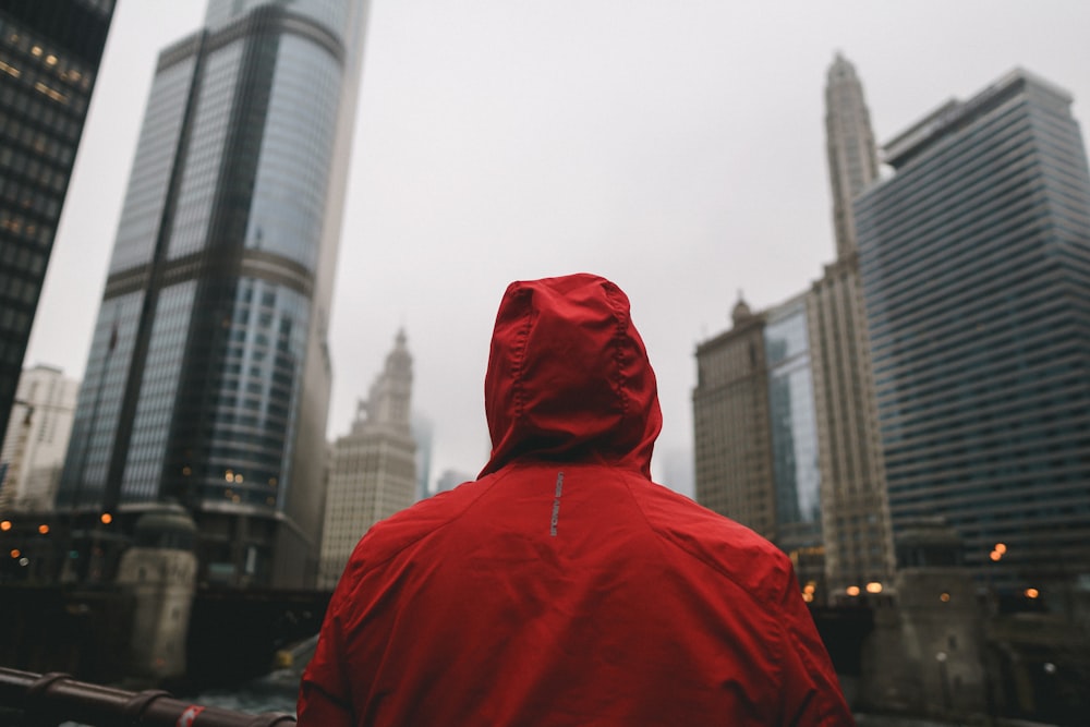 Persona con sudadera con capucha roja de pie frente a edificios de gran altura