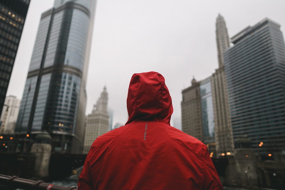 Persona che indossa una felpa con cappuccio rossa in piedi davanti a grattacieli