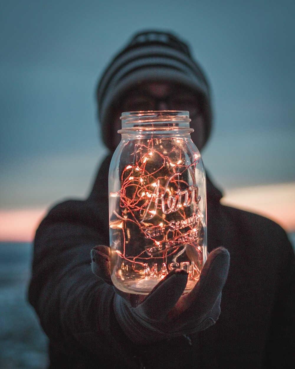 person holding glass mason jar with string lights