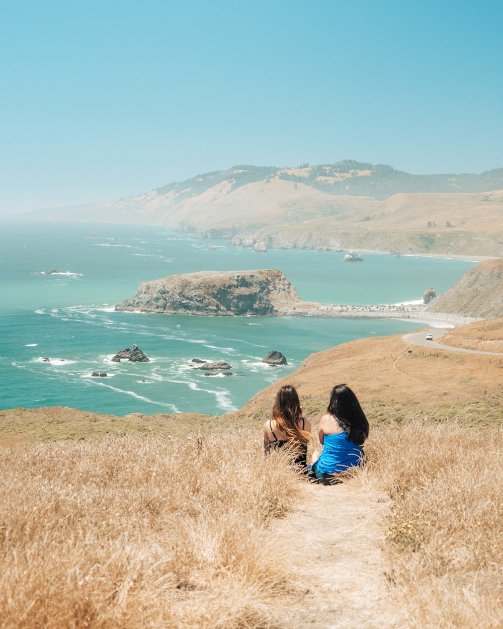 山と海に面した茶色の芝生に座る二人の女性