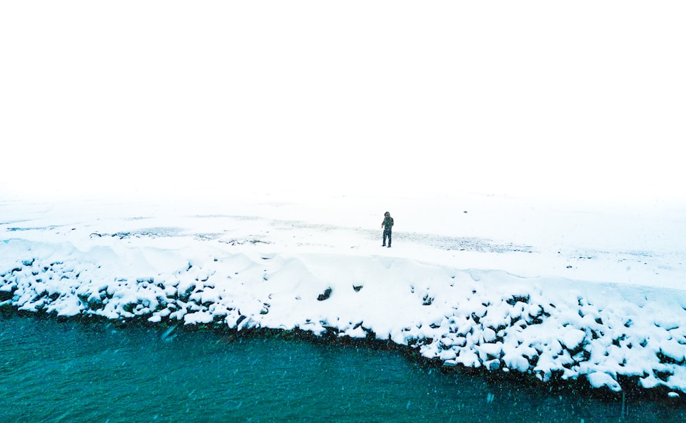 man standing at snowfield near body of water
