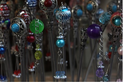 A collection of intricate hairpins features colorful beads and ornate metallic designs. The beads are in various colors including blue, green, red, and purple, and are paired with silver metalwork that adds an elegant touch.