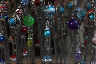 A collection of intricate hairpins features colorful beads and ornate metallic designs. The beads are in various colors including blue, green, red, and purple, and are paired with silver metalwork that adds an elegant touch.