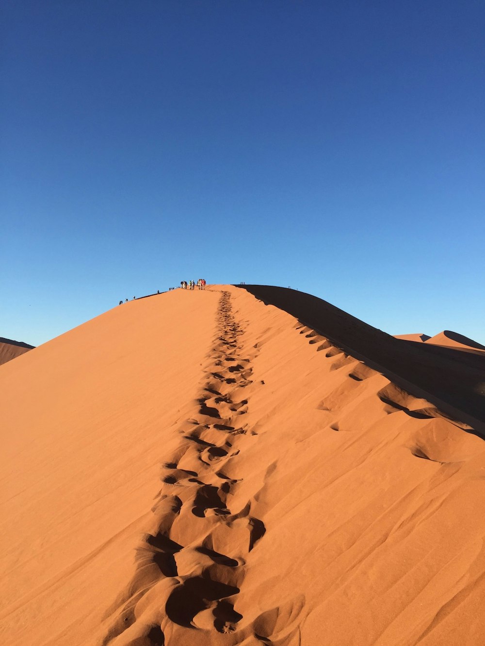 photo of foot prints on desert hill during daytime