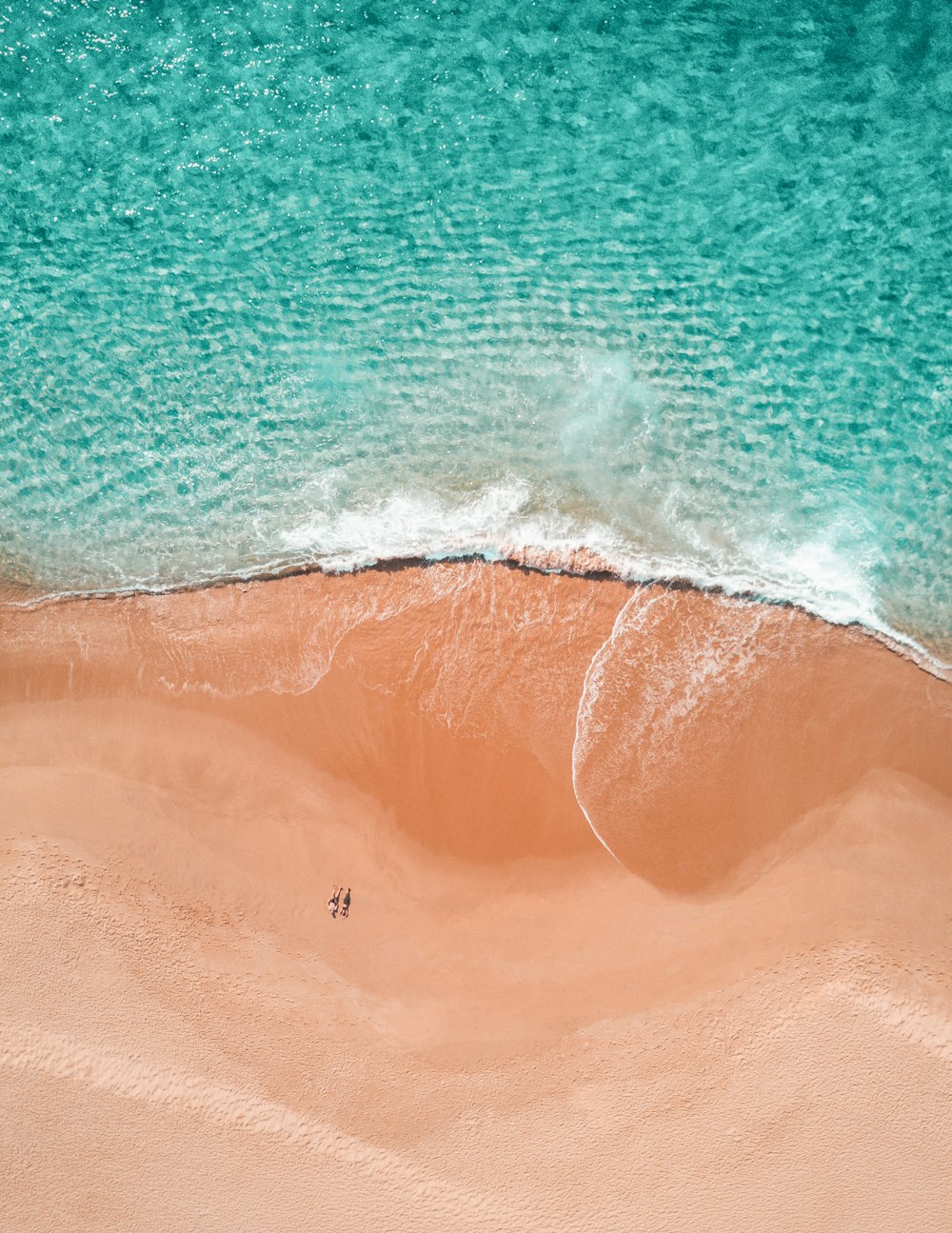 Fotografía aérea de dos personas tomando el sol en la orilla del mar