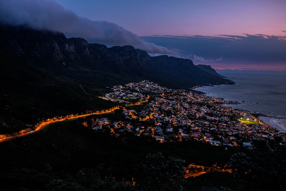 fotografia ad alto angolo della città vicino alla montagna fumosa e allo specchio d'acqua durante il tramonto