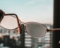 A close-up of eyeglasses with a modern frame reflecting city lights at dusk.