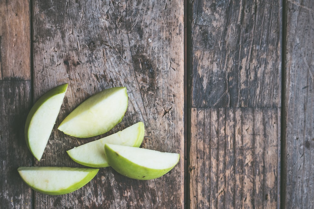 five green apple slices on brown wooden panel