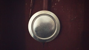 A silver metallic plate is attached to a dark brown surface, possibly a wooden door or wall. The plate is slightly tarnished, adding a rustic feel to the setting.
