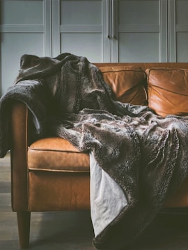brown leather sofa with a fuzzy brown and grey blanket draped over the arm of the sofa