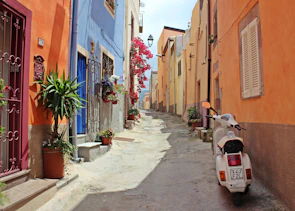 A charming narrow street in Siracusa lined with colorful buildings and blooming flowers.