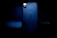 A smartphone with a sleek design is prominently featured in low light, focusing on its back side which displays the logo of a popular technology company. The surrounding is dark, creating a spotlight effect on the device.