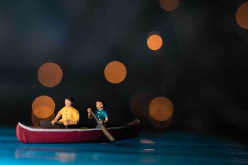 Fotografía bokeh de dos hombres montando canoa modelo a escala