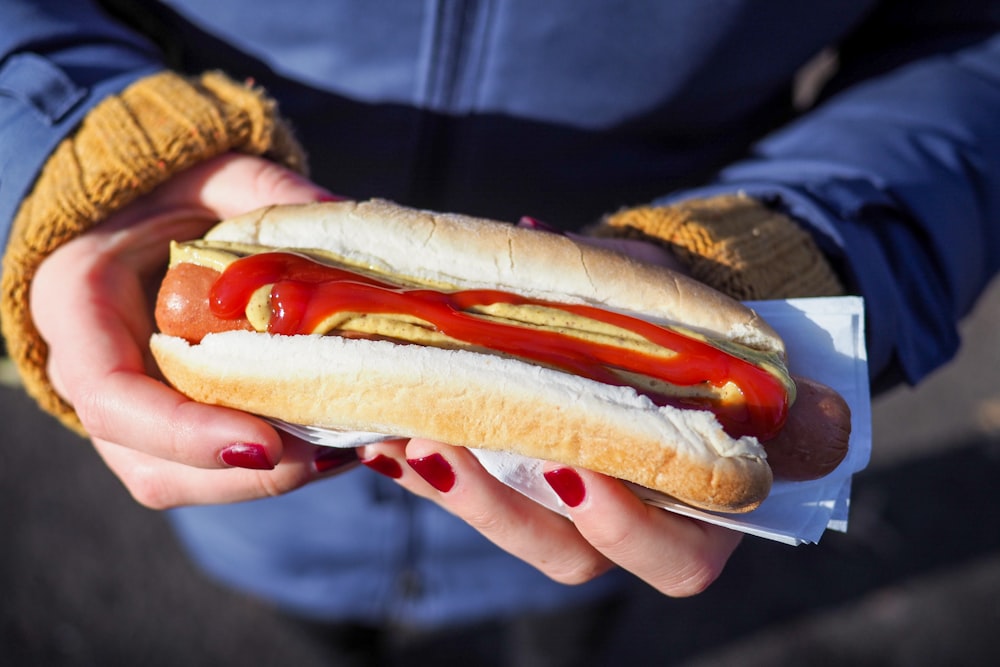 Person mit Hotdog mit Brötchen