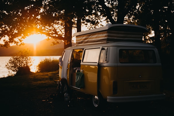 The van parked beside a serene lake at sunset, with speakers and turntables visible through the open door