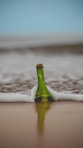 green glass bottle with cork lid on shore