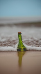 green glass bottle with cork lid on shore