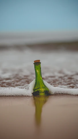 green glass bottle with cork lid on shore