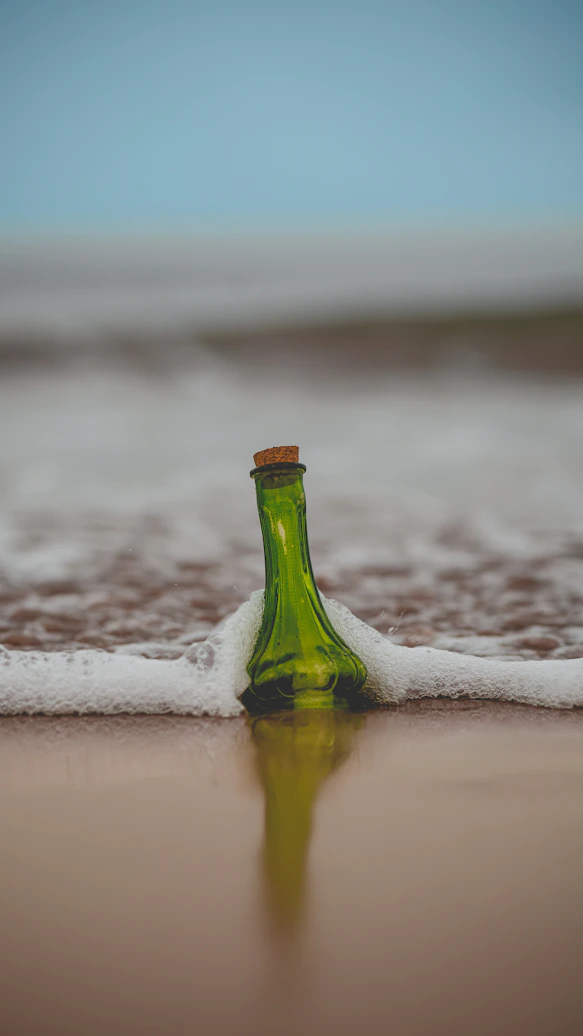 green glass bottle with cork lid on shore