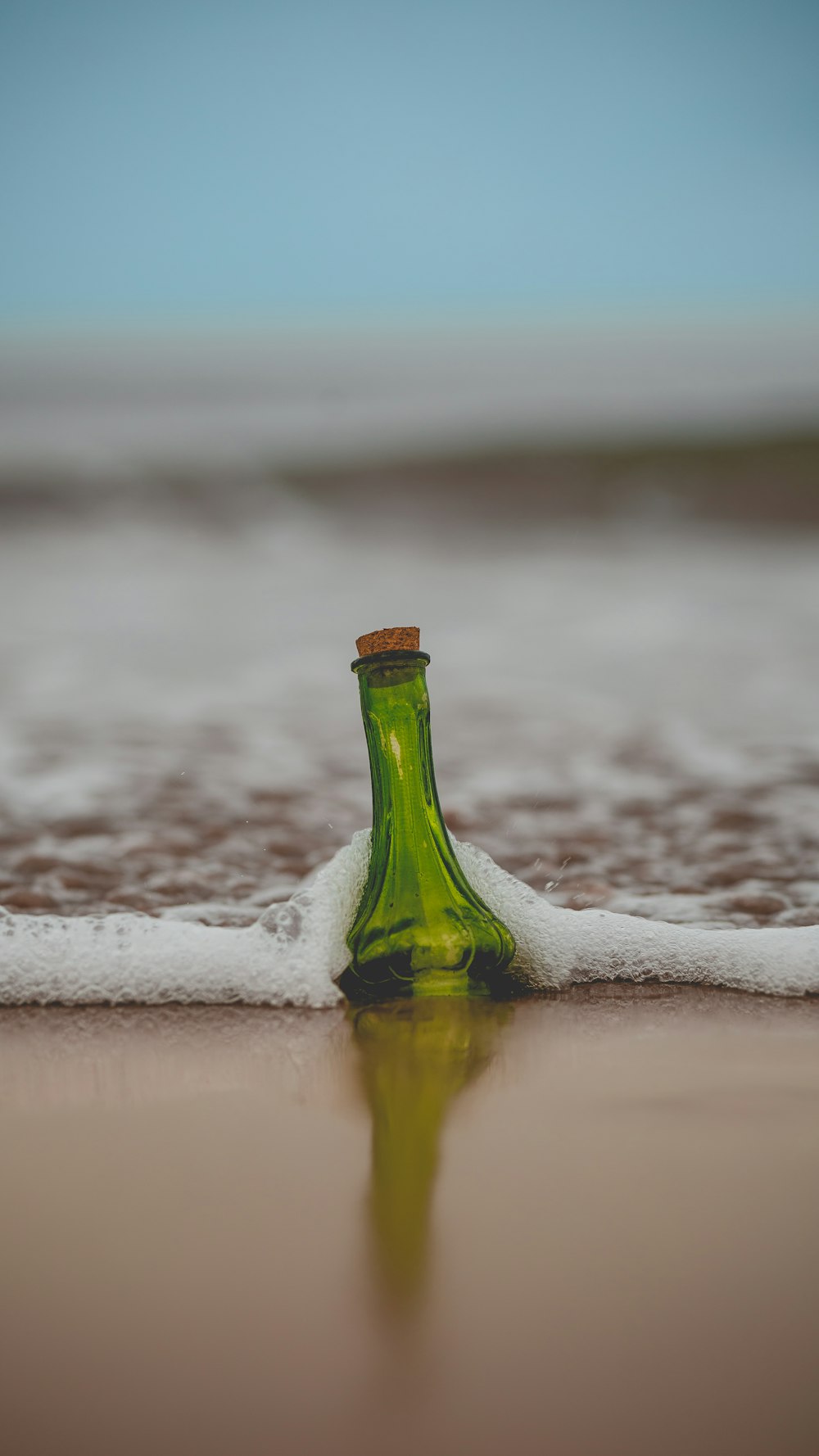 green glass bottle with cork lid on shore