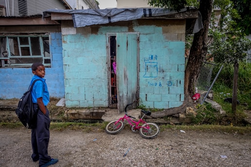 um menino pobre em frente sua casa velha.